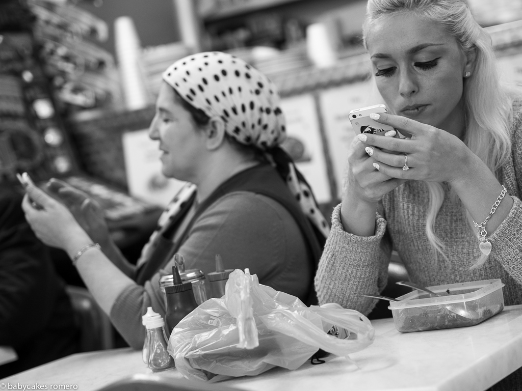 Two women at a café table, each absorbed in their phones